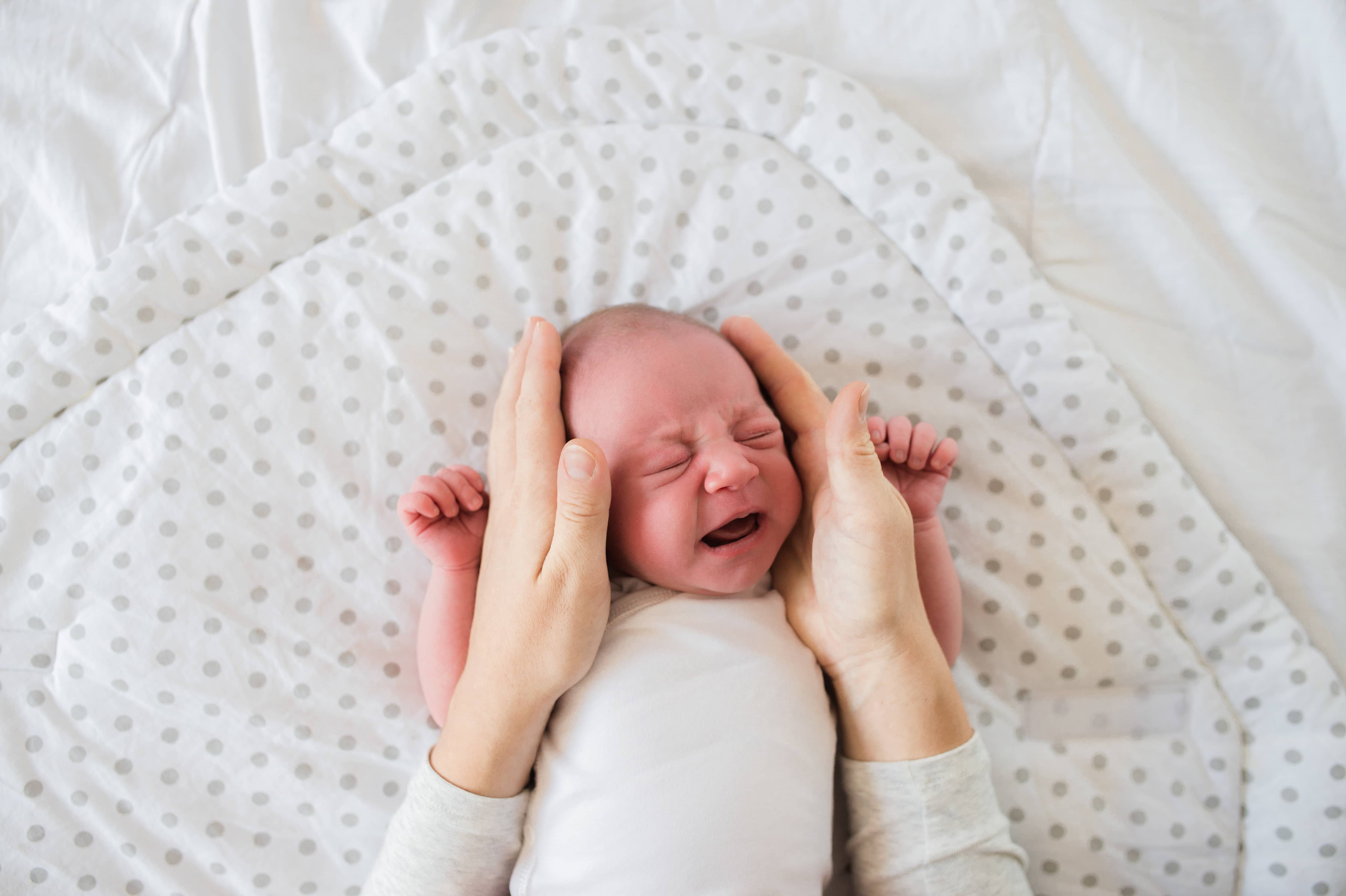 A pair of hands holding a newborn baby's head while it cries