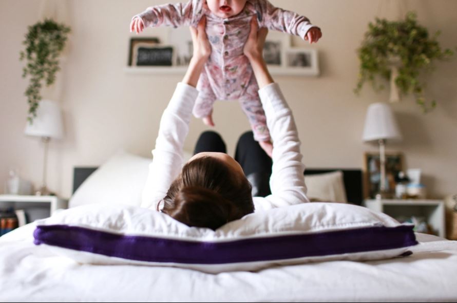 Mom lying on her back on her foam pillow carries her baby in her arms
