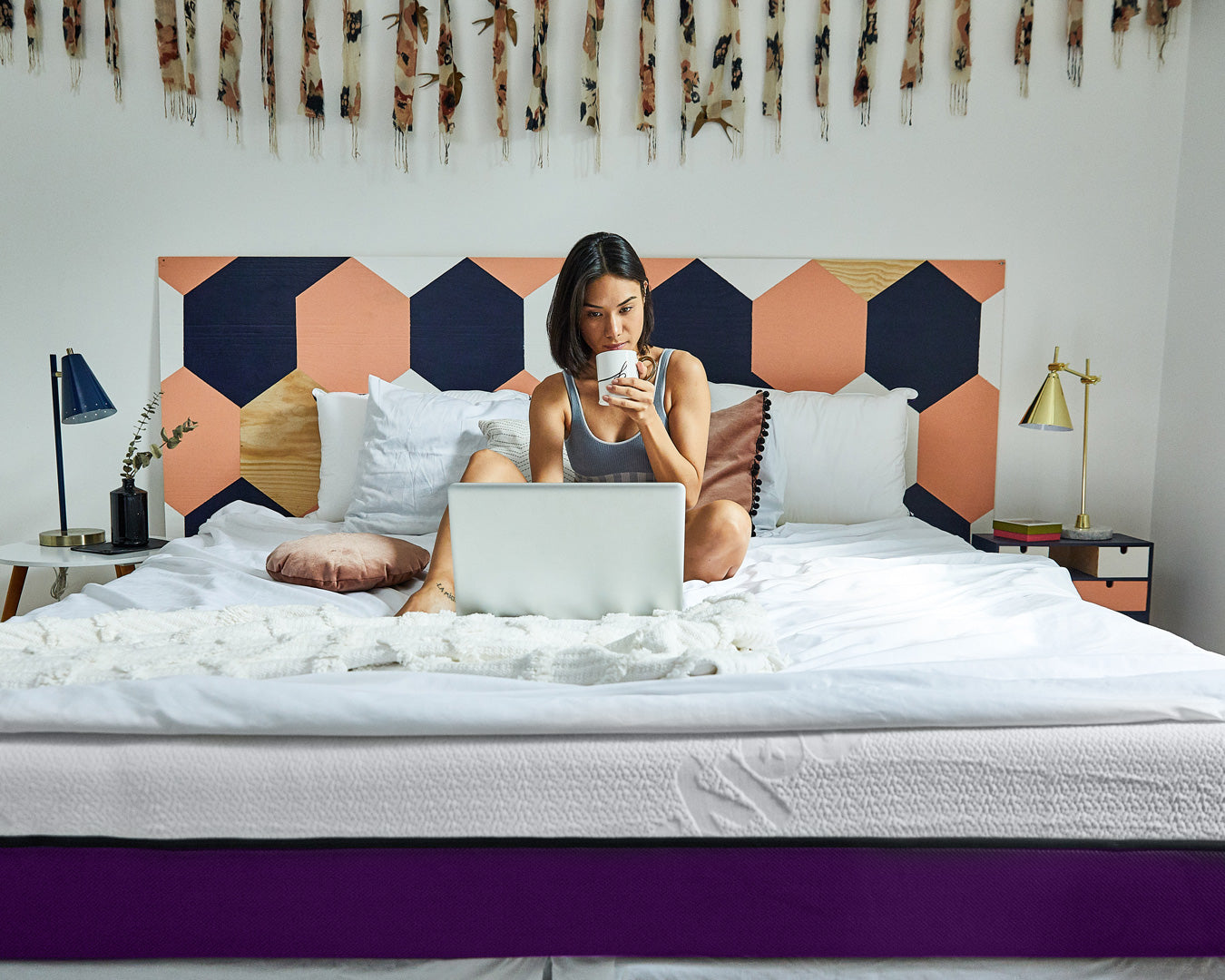 Une Femme boit dans une tasse assise sur son lit et commande un matelas en mousse Polysleep