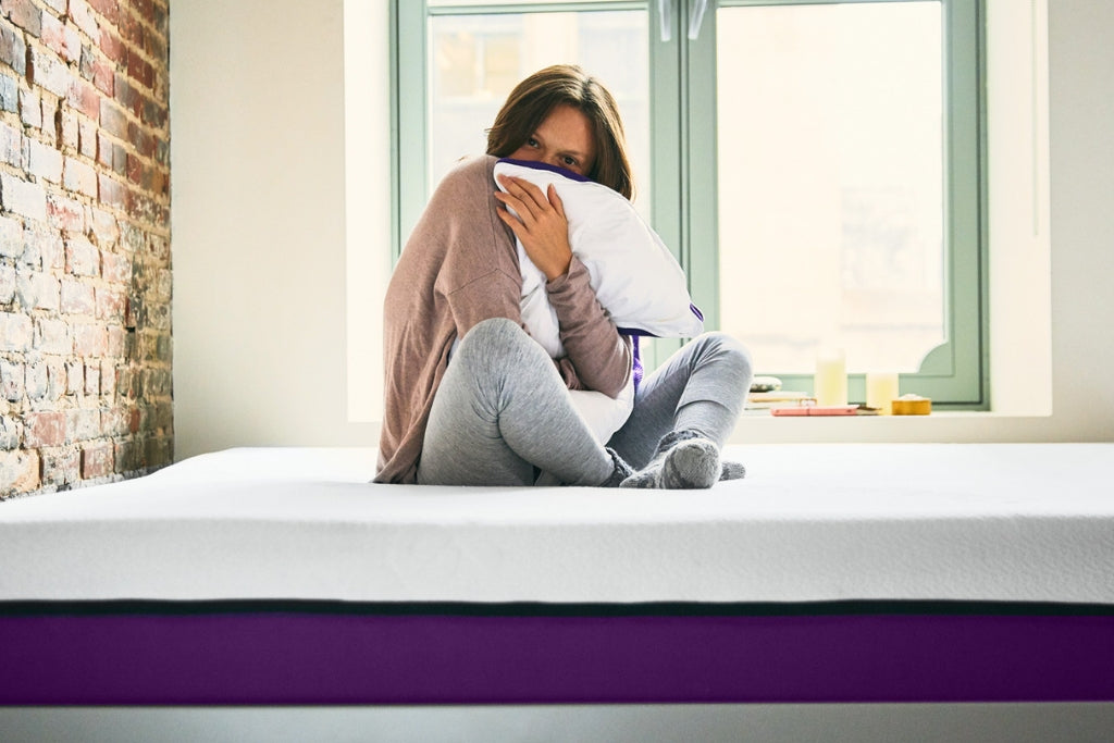 A Woman holds her Polysleep pillow in her arms while sitting on her Polysleep foam mattress