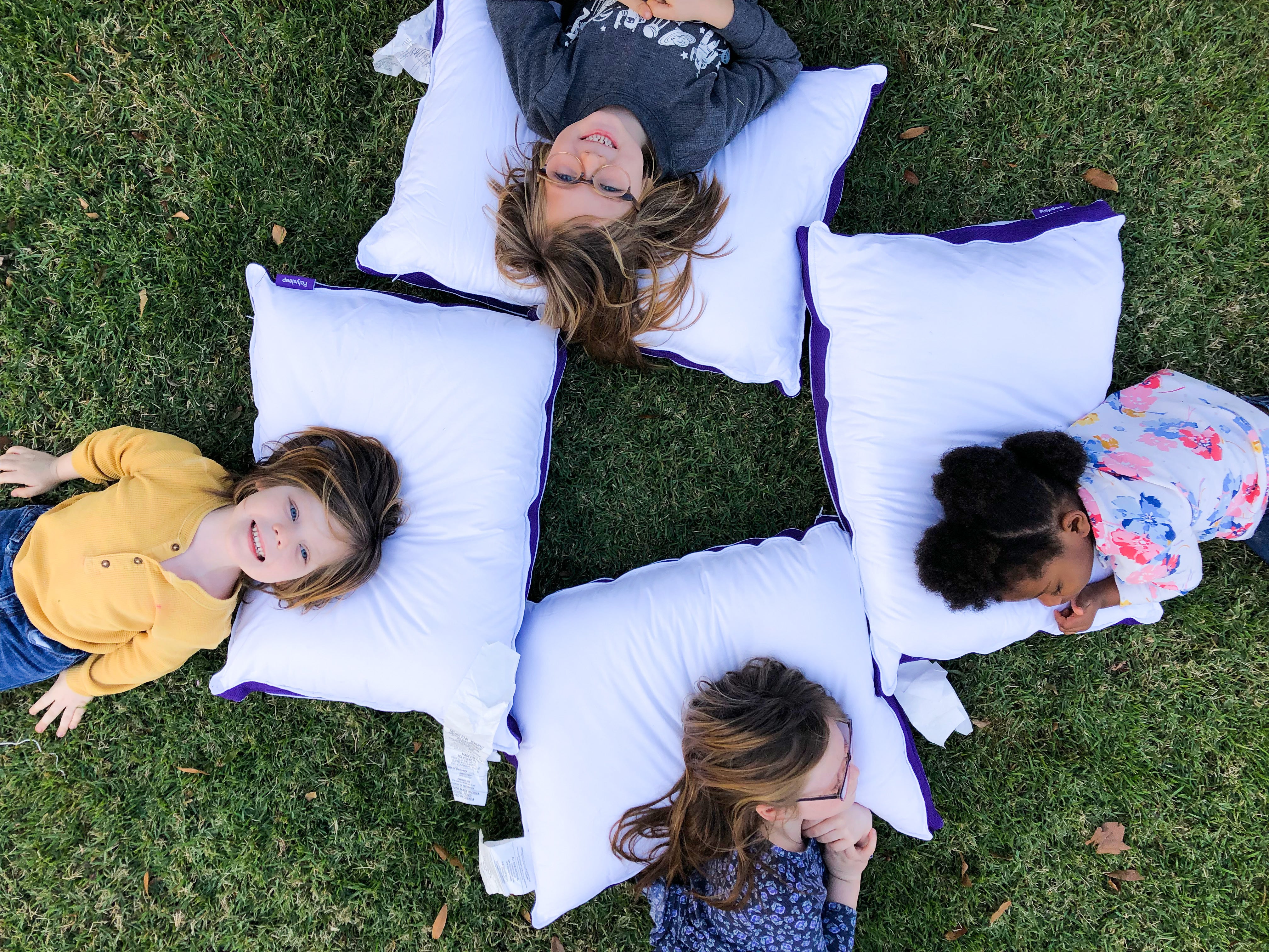 4 petites filles sont allongées sur leurs oreillers Polysleep dehors sur la pelouse